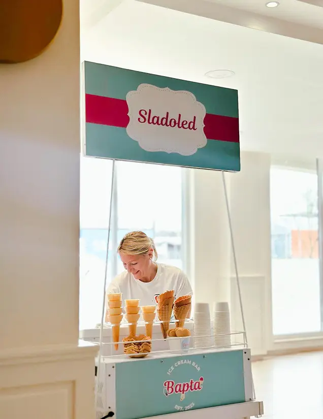 zena stoji sa sladoledom i friziderom i nasmejana je